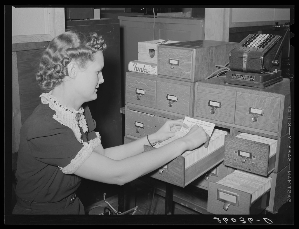 A clerk filing record cards in a wooden card index cabinet, 1940s