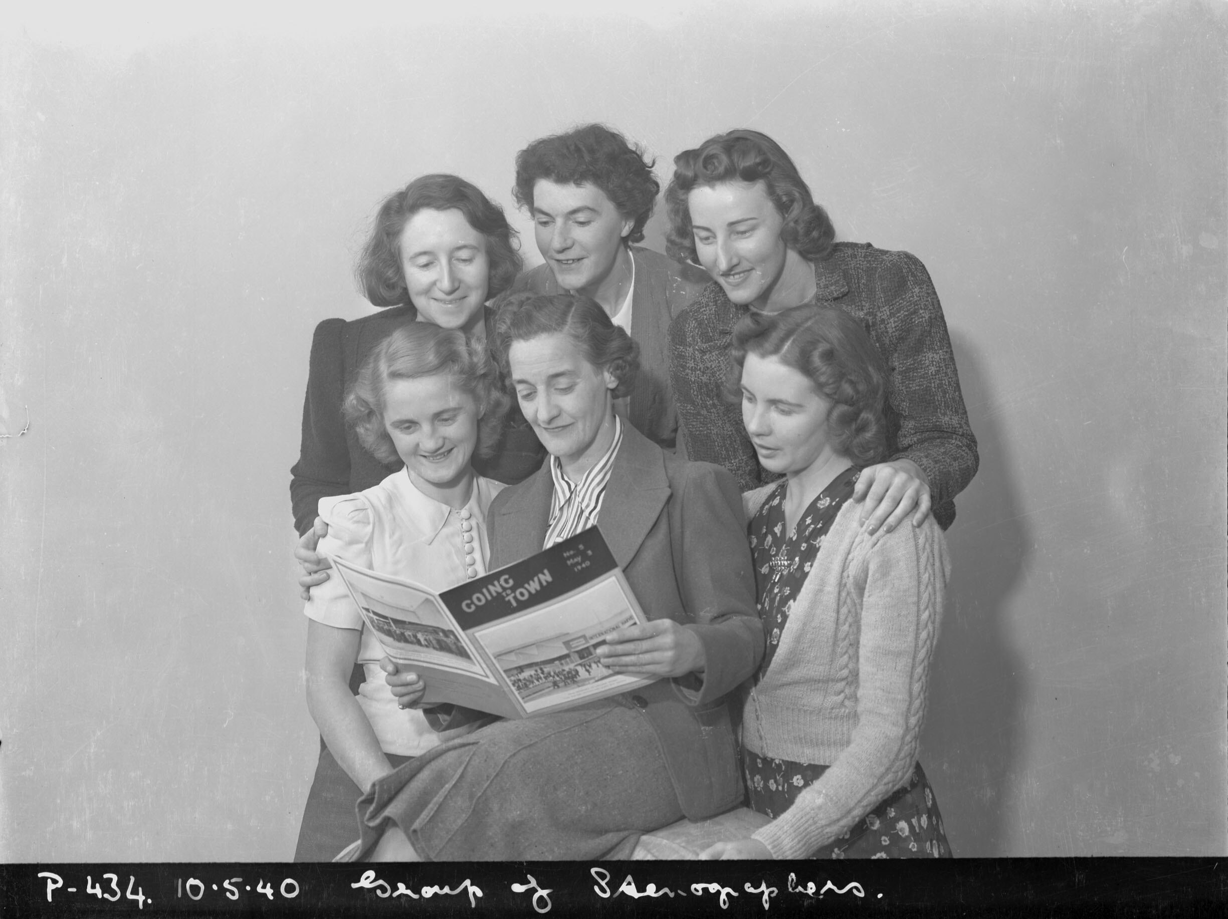 Six office workers gathered around one booklet, reading it together, 1940