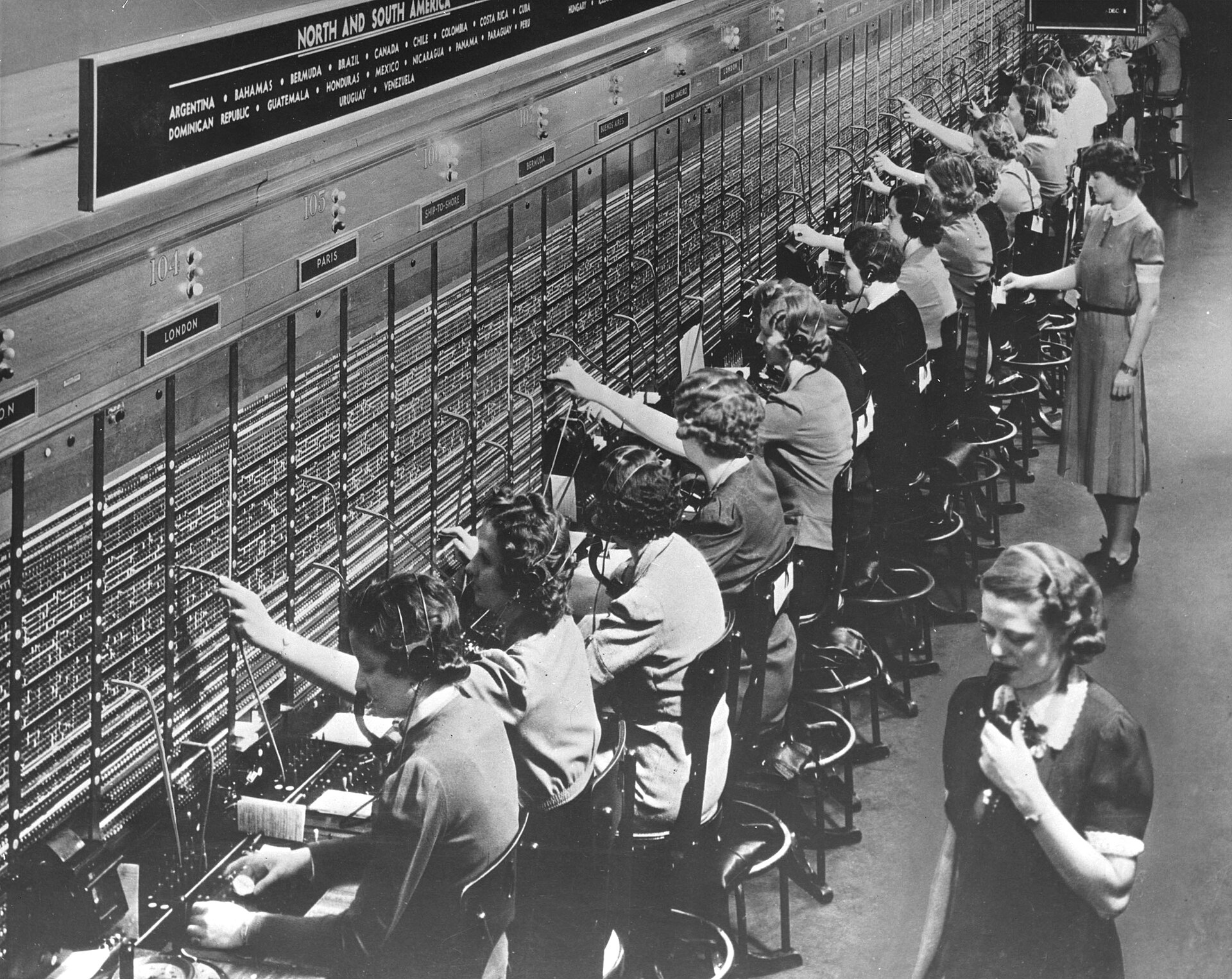Rows of telephone operators at a Bell System switchboard, connecting each call by hand with plug cords